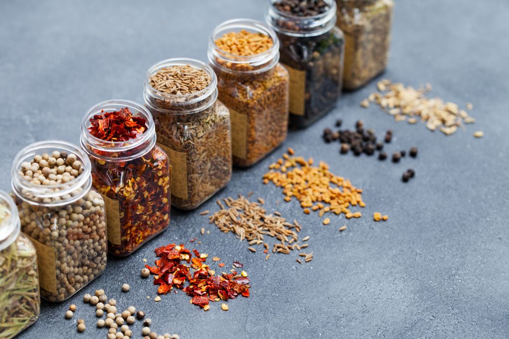 Assortments of spices, white pepper, chili flakes, lemongrass, coriander and cumin seeds in jars on grey stone background. Copy space